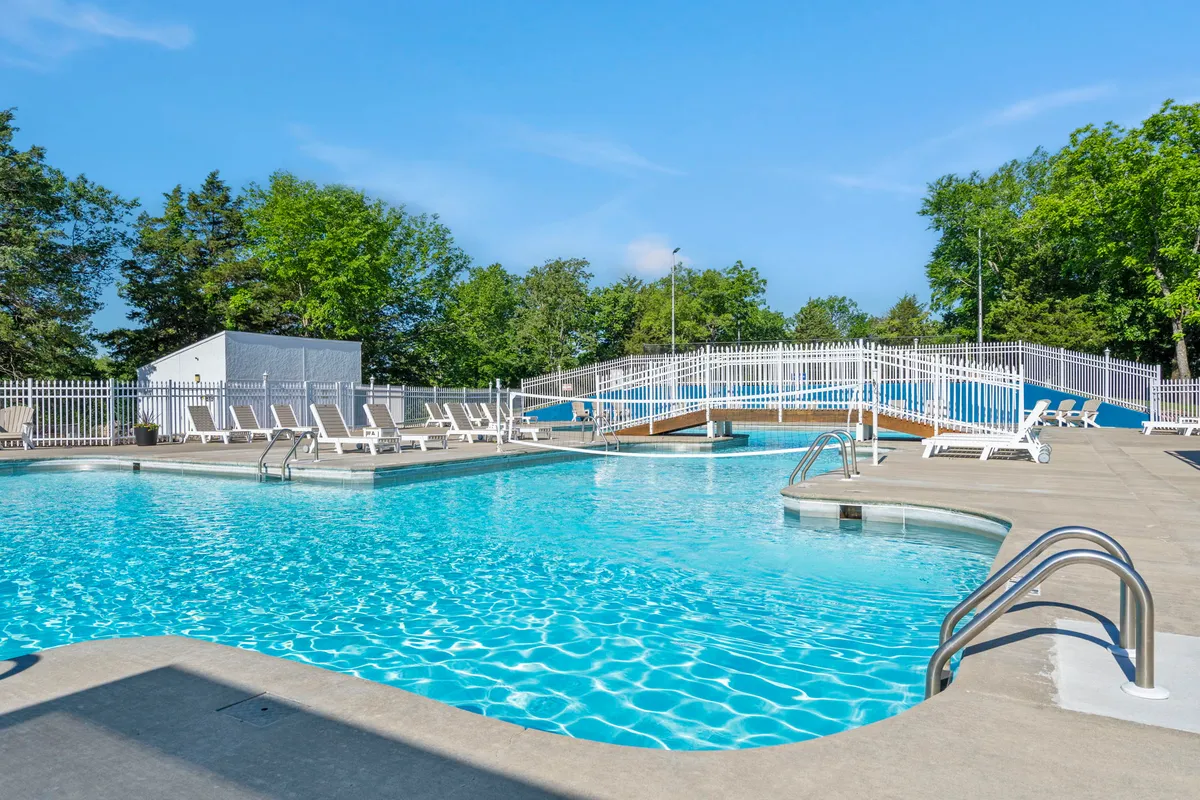 A sparkling swimming pool with sun loungers and a small bridge, nestled in greenery, offering a space for relaxation, swimming, and social gatherings.
