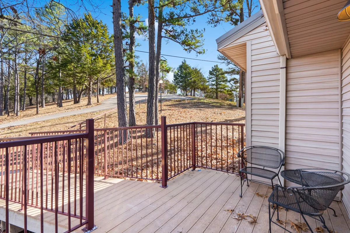 An exterior deck area surrounded by trees, featuring metal chairs and a pathway leading into nature. The setting is ideal for pets to explore, bask in the sun, or enjoy the fresh air with their owners.