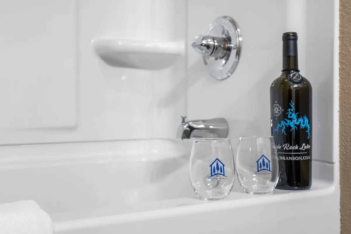 A bright, inviting ensuite bathroom with a large bathtub, a bottle of wine, and two glasses set nearby, suggesting a space designed for relaxation and pampering. The mood is peaceful, perfect for unwinding after an active day.