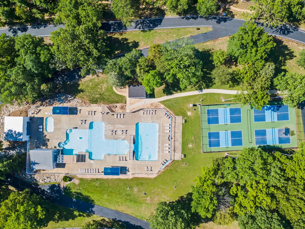 This exterior image features a sparkling swimming pool surrounded by lush greenery and tennis courts in the background. The pool is ideal for both children and adults, with ample space for sunbathing, swimming, and relaxing. The natural surroundings give a sense of the resort's inviting outdoor amenities.