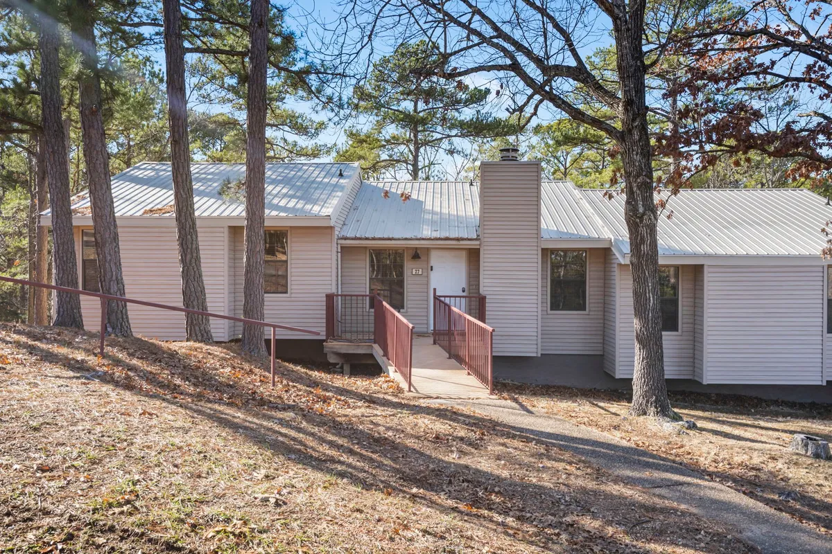 An inviting front porch with steps leading up to the entrance, surrounded by mature trees and greenery. The porch is set up for relaxation, suggesting a welcoming atmosphere and direct access to outdoor spaces.