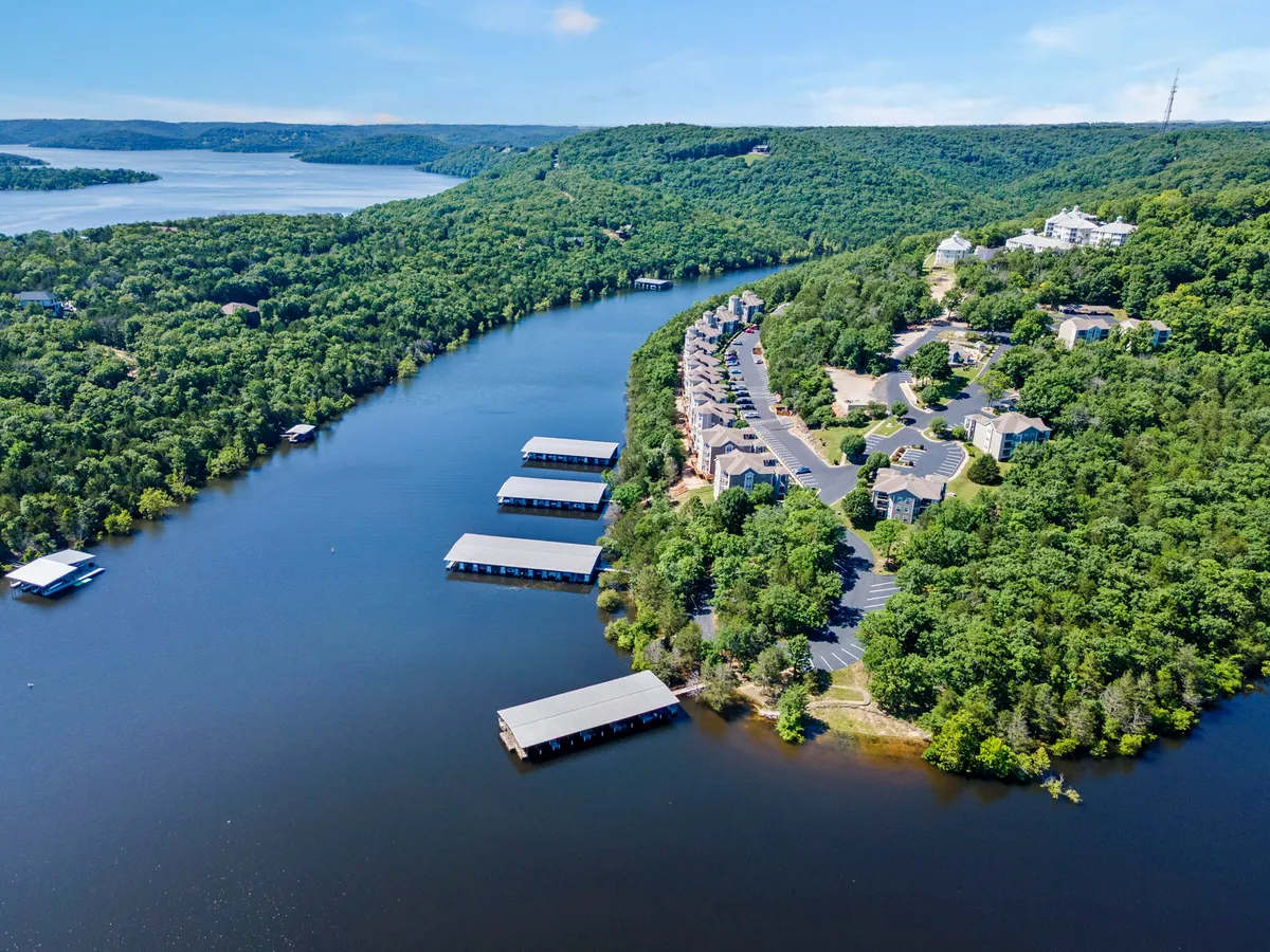 This image captures a calm river scene with lush greenery, marinas, and residential buildings along the shoreline. The atmosphere is peaceful, and the image suggests easy lake access and opportunities for boating, fishing, and hiking. The light appears to be soft, possibly during sunset, enhancing the sense of relaxation and recreation by the water.