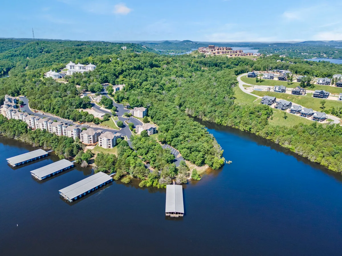 A panoramic view over a tranquil lake and marina, framed by residential buildings, rolling hills, and roadways. The scene suggests a welcoming community and multiple opportunities for lakeside activities and gatherings.