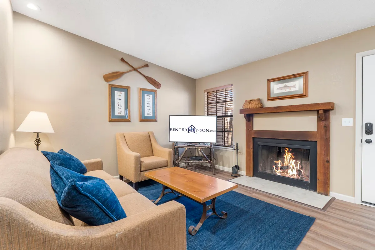 The image captures a cozy living area featuring a charming stone fireplace, plush sofa, rustic coffee table, and playful decorative oars on the wall. The warm lighting and inviting ambiance suggest a perfect space for families or couples to unwind, with a television ready for movie nights and comfortable seating ideal for relaxing or socializing.
