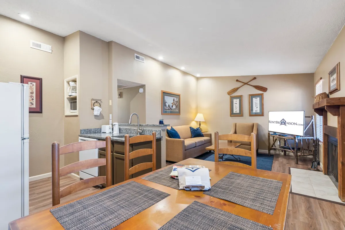 A spacious open-concept living and dining area featuring a cozy sofa, a dining table set for family meals, a fireplace as the focal point, and a television for entertainment. The room exudes a welcoming, homely atmosphere with comfortable furnishings and warm lighting.