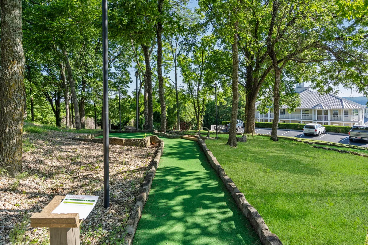 A playful scene of the resort's mini-golf pathway winds through trees, with colorful signage and a glimpse of the parking area. The area is welcoming and tailored for family gatherings, picnics, and learning mini-golf together.