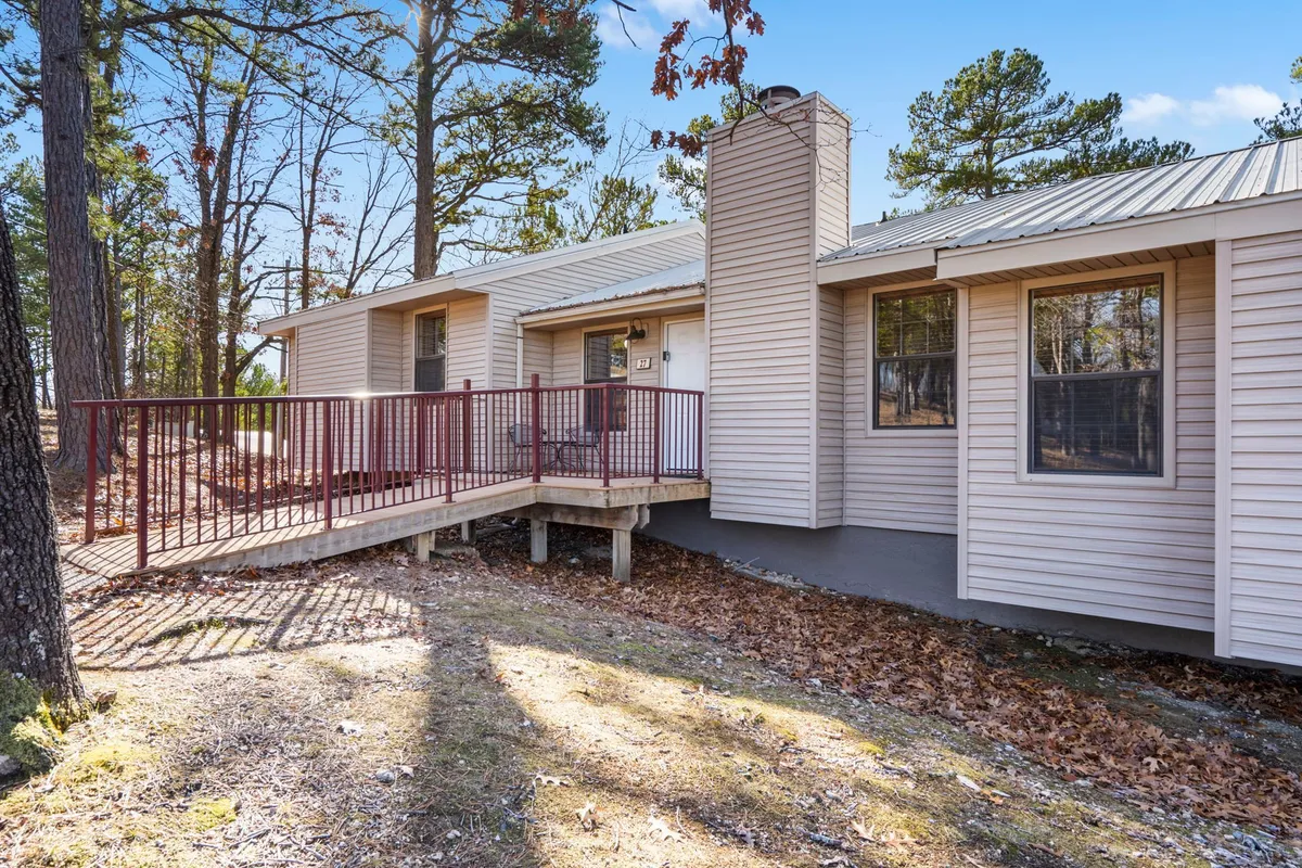 A welcoming deck with seating, the entrance door, a chimney, and lush trees surrounding the space. The deck offers a peaceful vantage point with glimpses of nature, ideal for morning coffee or stargazing.