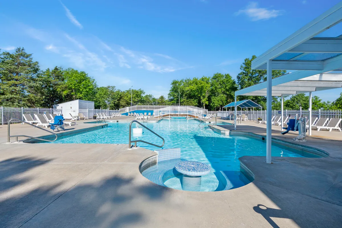 A spacious swimming pool area surrounded by lounge chairs and a nearby hot tub, set against a backdrop of lush greenery. The inviting space is ready for group relaxation, sunbathing, or lively poolside gatherings.